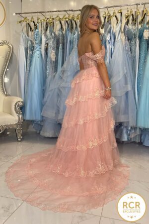 A blush off the shoulder corset style bodice with a layered ruffle A-line skirt and a leg split.