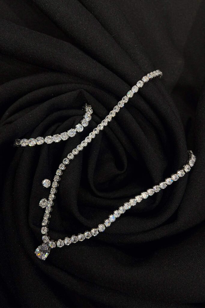 A silver white square-stone necklace with a tear-shaped pendant and a fold over clasp, a matching bracelet, and studs.
