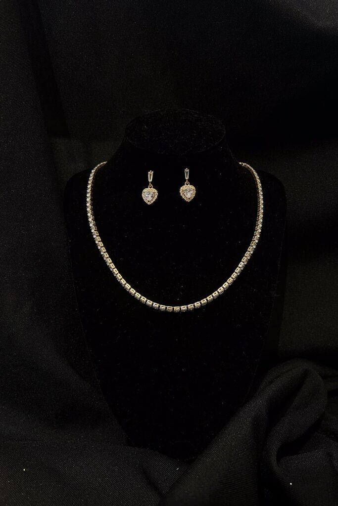A gold square-stone necklace with a fold over clasp, a matching bracelet, and studs with a heart-shaped pendant. Both chain and bracelet contain an extension.